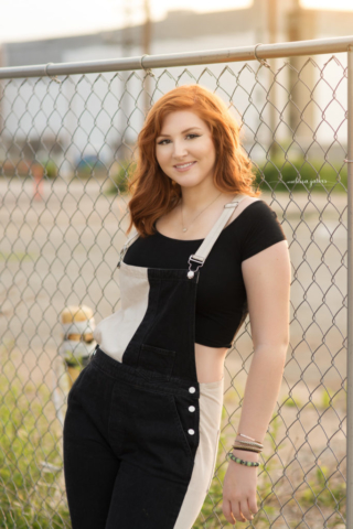 red headed north allegheny high school senior poses against a fence during her urban senior portrait session in pittsburgh pa
