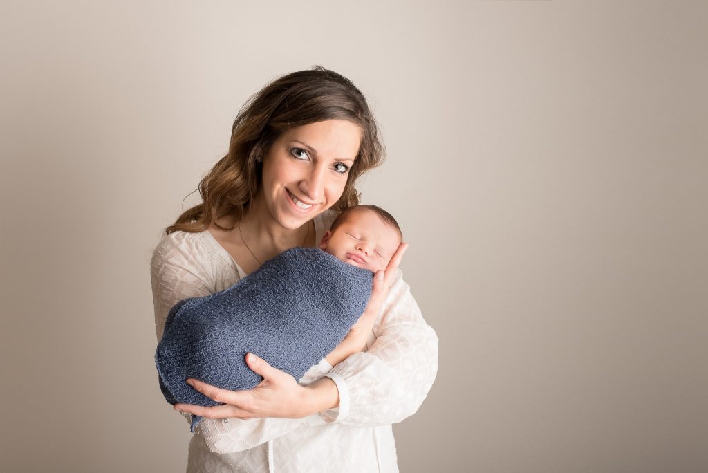 A mother proudly holds her son while wrapped in a blue swaddle during their newborn portrait photography session in Pittsburgh, PA