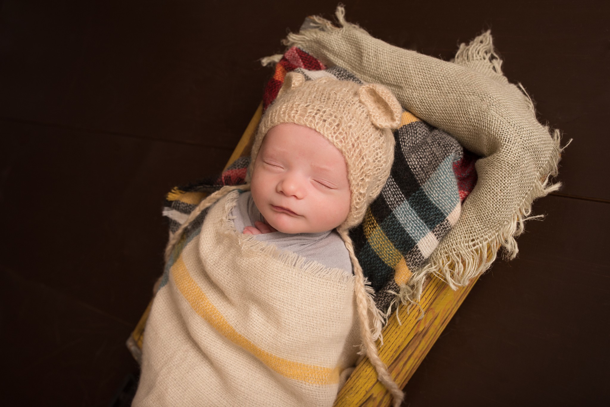 A baby boy wrapped in a fall burlap and plaid blanket wearing a knit hat during a newborn portrait photography session in Cranberry Twp Pittsburgh PA