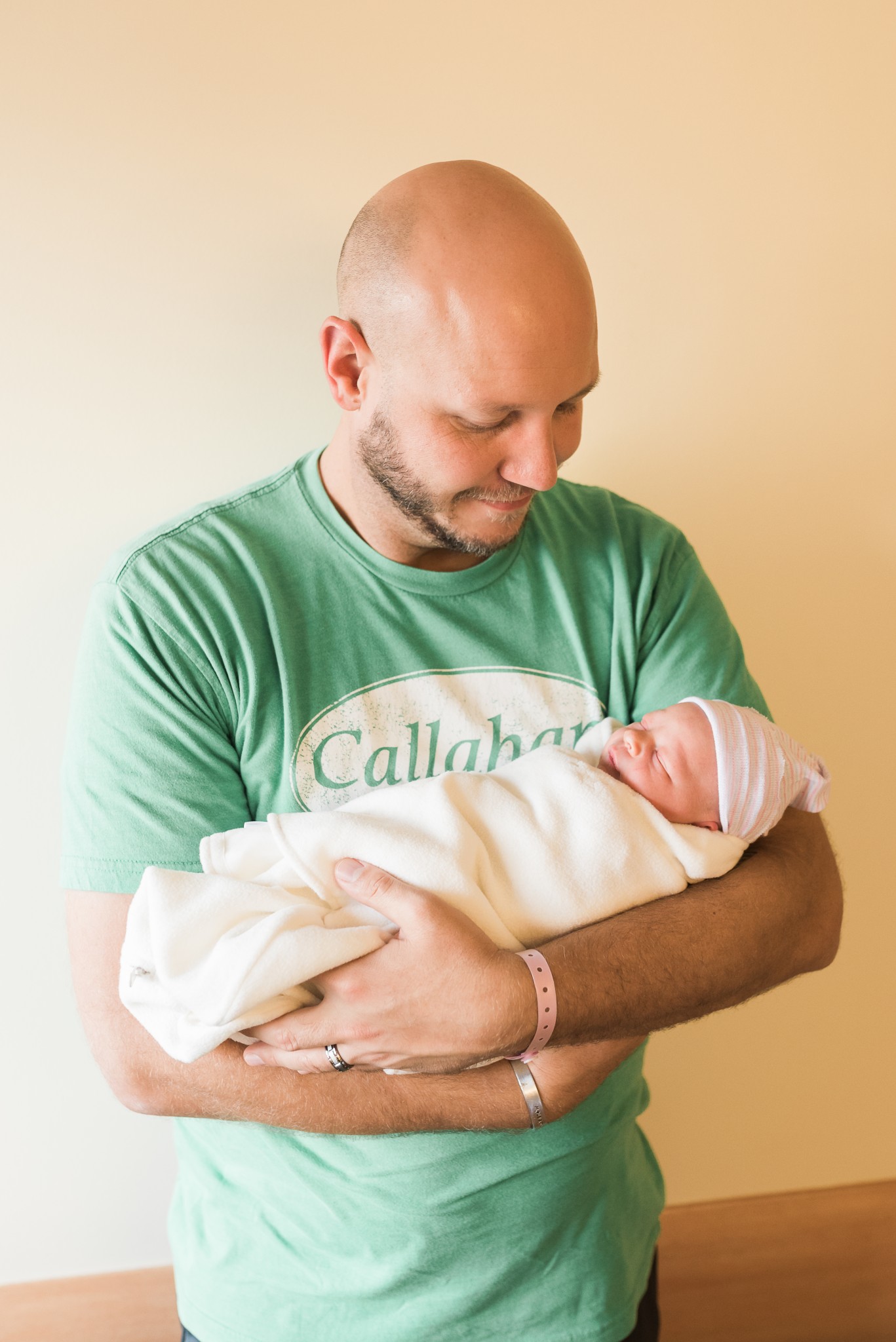 A dad wearing a green t shirt holds his daughter in a white wrap during a Fresh 48 In Hospital Newborn portrait photography session in West Penn Hospital which is in the Pittsburgh area.