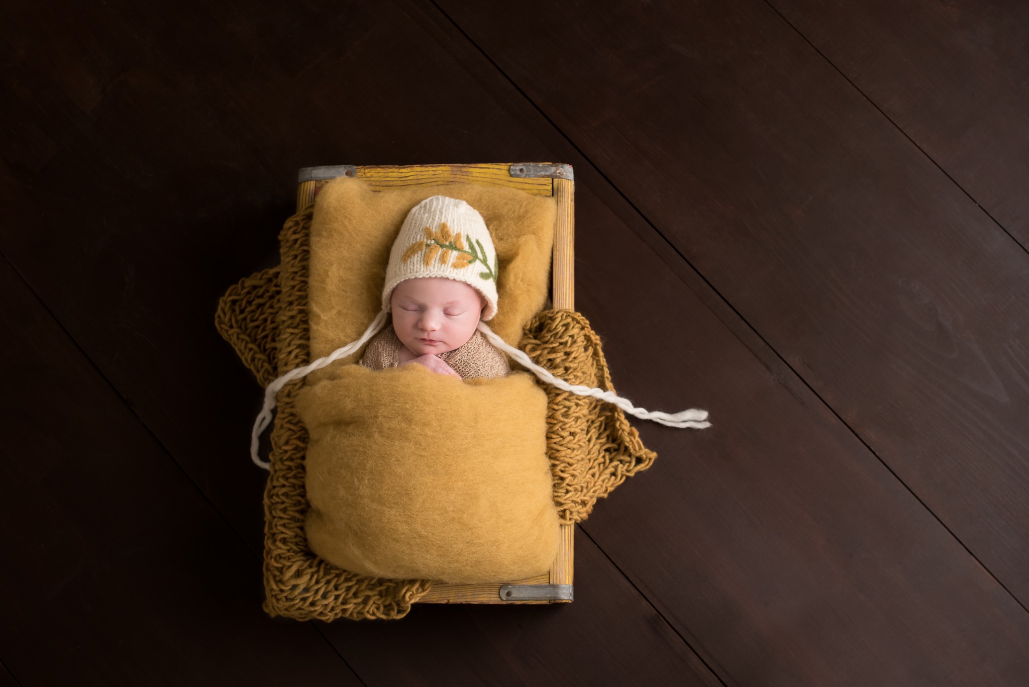 A baby girl rests in mustard gold fabrics and knits in a vintage crate with a goldenrod bonnet during her Pittsburgh newborn photography session in Cranberry Twp PA