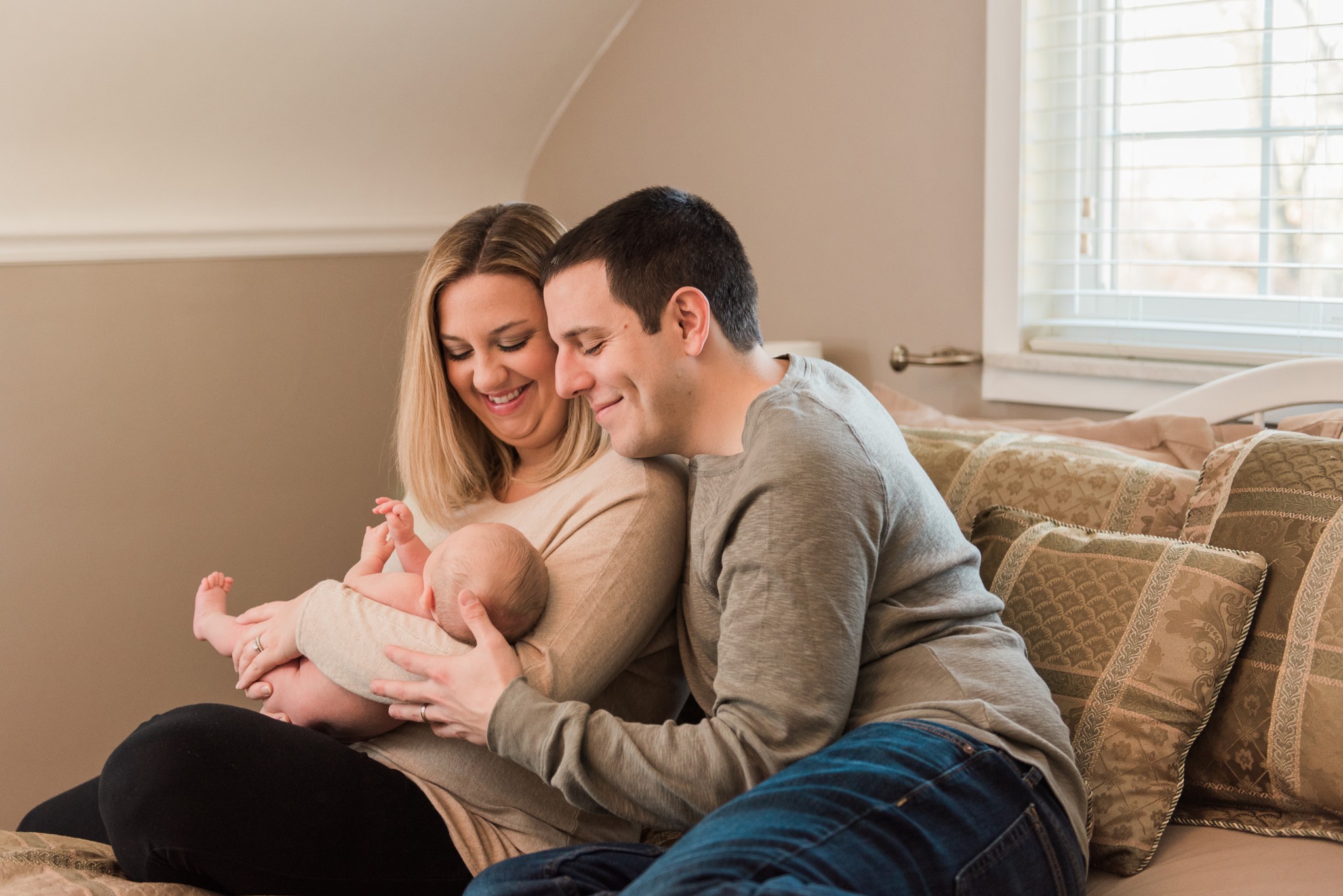 A baby boy is held by his mother and father on their bed for their in home lifestyle photography session in the Pittsburgh area.