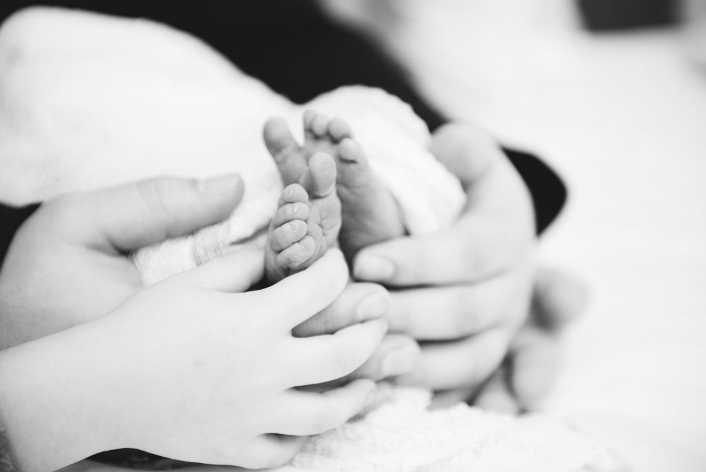 Baby feet surrounded by hands of his brother and father during their photography session in a Pittsburgh hospital.