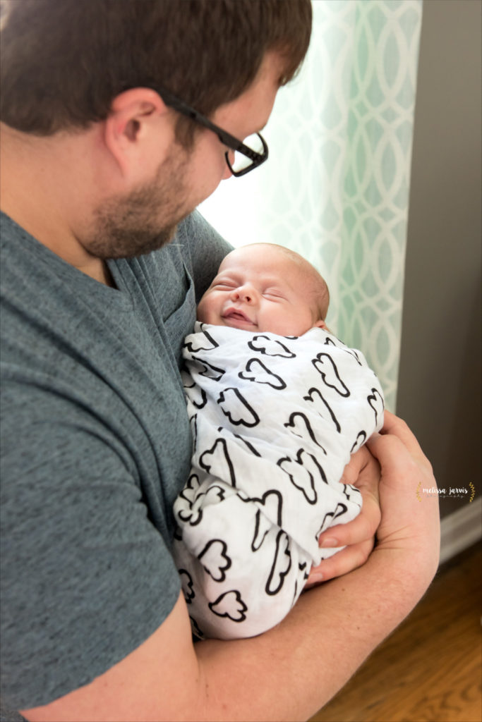 A newborn baby boy smiles at his father while wearing a white swaddle during his newborn in home lifestyle photography session in Cranberry Twp Pittsburgh PA
